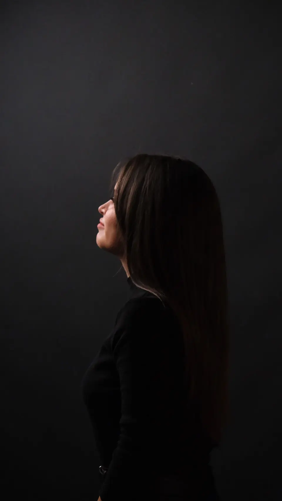 Seated studio portrait of a woman in a dark high-necked top, turned away from the camera