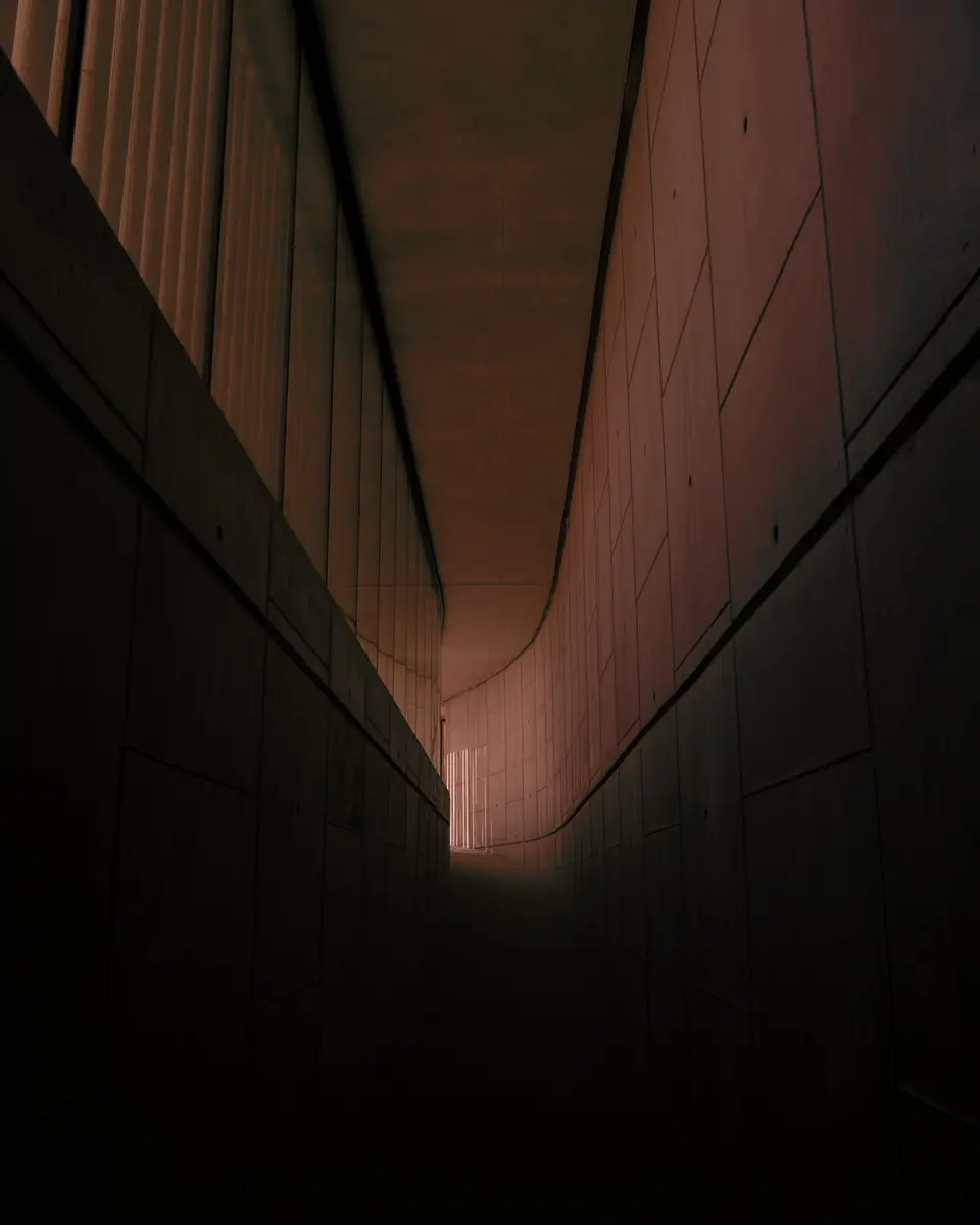 A long, dimly lit concrete corridor with daylight falling across the floor